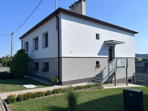 Rodinný dům s bílou fasádou, šedým soklem a venkovním schodištěm